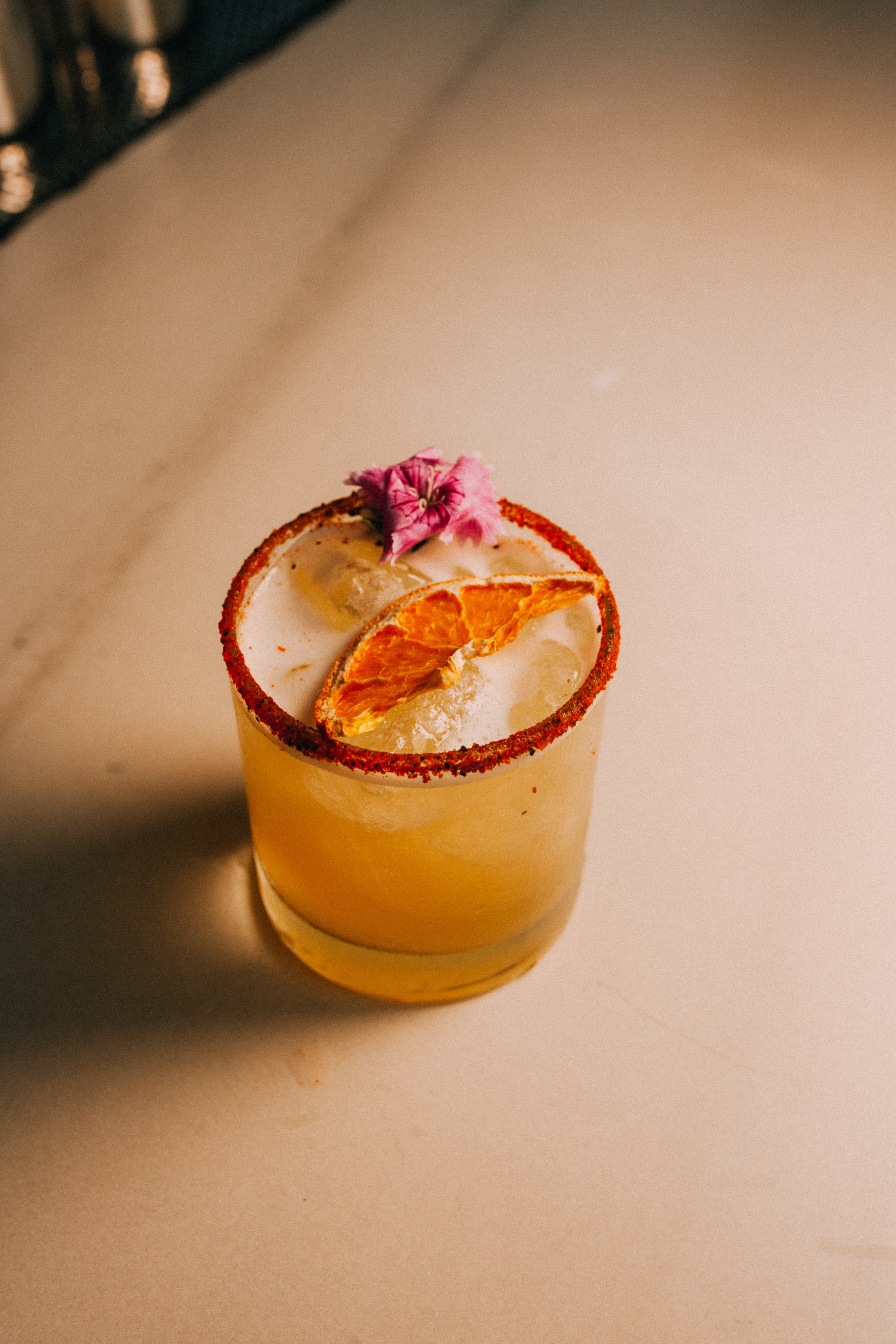 Signature cocktail with dried orange and a pink edible flower on marble